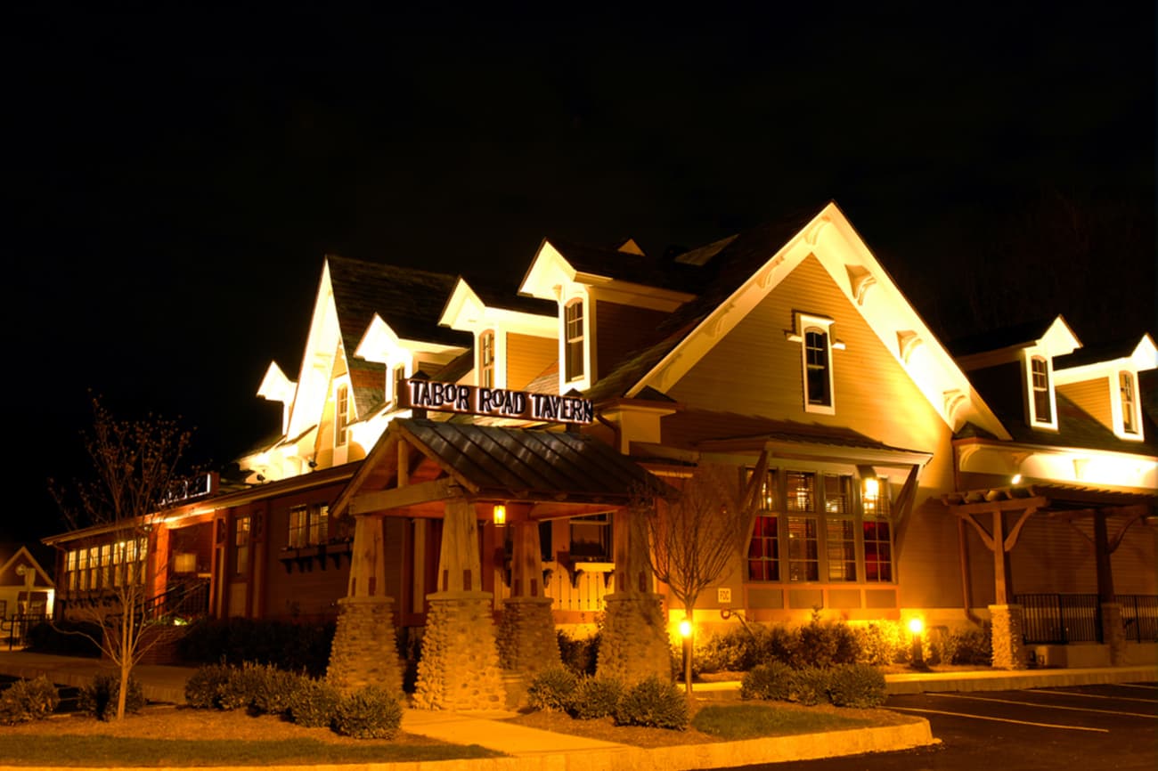 Tabor Road Tavern lit up at night, its multi-gabled roofline above the entrance sign
