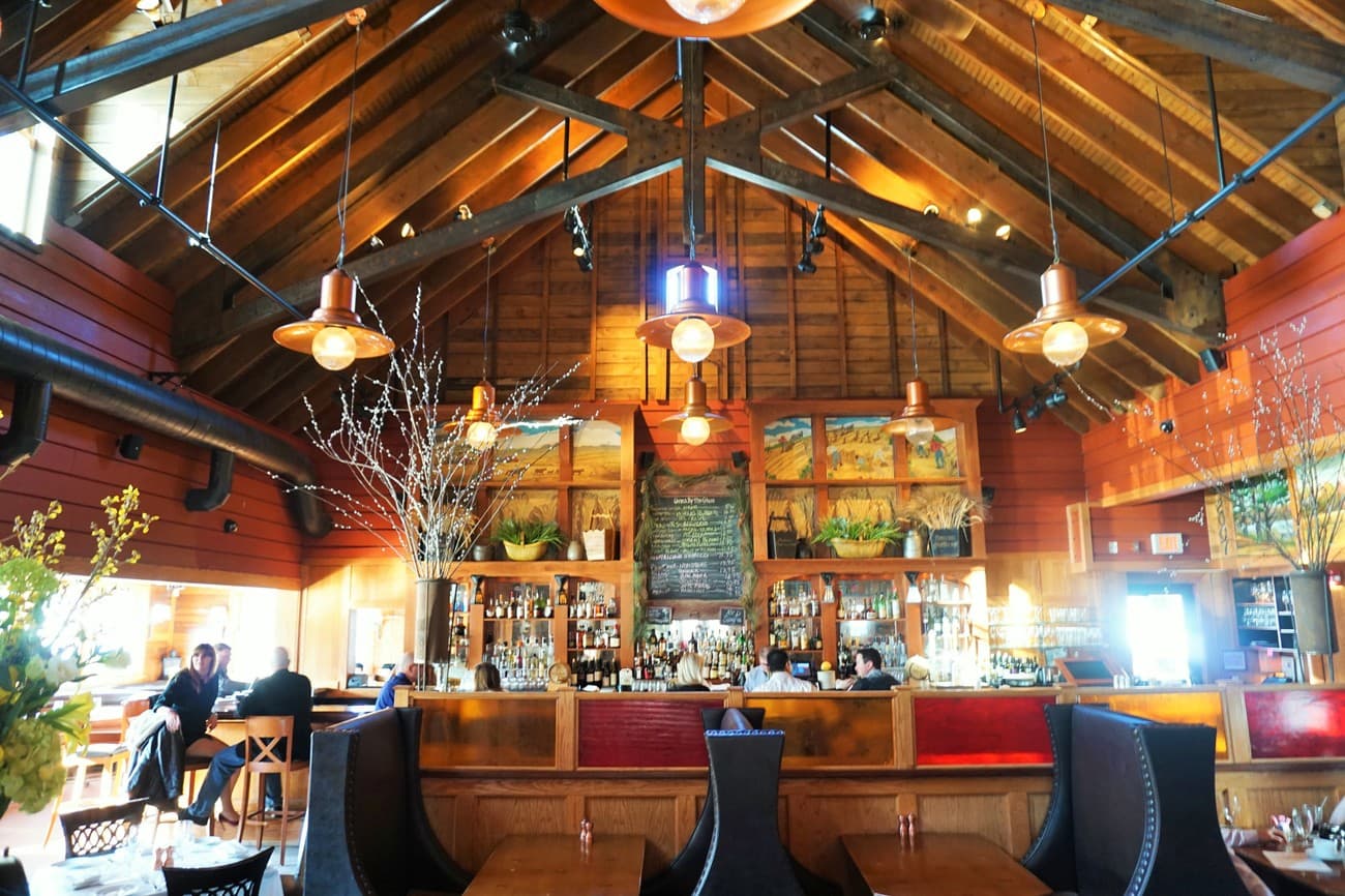The dining room under a vaulted wood ceiling with exposed trusses and copper pendant lights